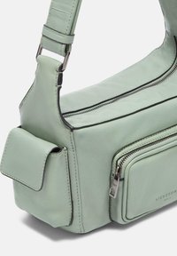 Sac à épaule en cuir vert clair avec une finition texturée, doté d'une poche zippée, d'une bandoulière réglable et d'accents de couture noire contrastants.