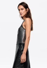 Srebrny, bezrękawnik z cekinami o okrągłym dekolcie, zestawiony z czarną skórzaną spódnicą. Gładka faktura i dopasowany krój.