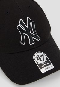 Svart baseballcap av stoff med en brodert hvit NY-logo. Inkluderer en sirkulær etikett som sier '47 MVP Justerbar.
