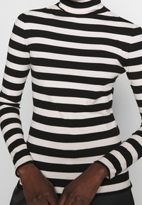 Maglione a maniche lunghe a righe bianche e nere con un design aderente e una texture a coste, caratterizzato da una larghezza delle righe contrastante.