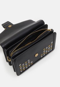 Borsa in pelle nera con due scomparti con zip, caratterizzata da occhielli in oro e argento su un lato e una chiusura a scatto.