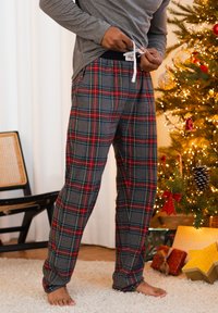 Grijze geruite pyjamabroek met rode en gele lijnen, voorzien van een elastische tailleband en trekkoord. Draagt een grijs longsleeve shirt.