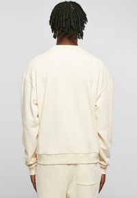 Cremefarbener Sweatshirt mit langen Ärmeln, Rundhalsausschnitt sowie Rippstrickbündchen und -saum. Hergestellt aus weichem Material mit glatter Textur.