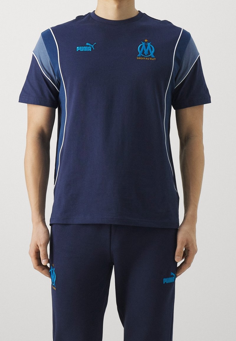 Mörkblå tränings t-shirt med korta ärmar, med ljusblå accenter och Puma-logga; inkluderar broderad Marseille-insignia på bröstet.