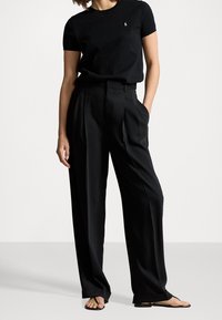 Černé bavlněné tričko s logem na hrudi, spárované s černými vysokými plisovanými kalhotami. Hladká textura a uvolněný střih.