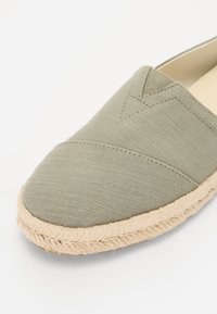 Olivgrüne Espadrilles mit einem Obermaterial aus strukturiertem Stoff und einer Sohle aus Jute. Verfügt über ein gesticktes Muster auf dem Stoff und eine runde Zehenpartie.
