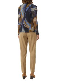 Langärmliges, gemustertes Oberteil in Marineblau, Braun und Blau; kombiniert mit beigen Hosen. Die Absatzschuhe haben ein dunkles, strukturiertes Akzent.
