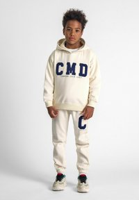 Cream hoodie with navy fleece lettering and matching joggers, featuring embroidered initials; paired with multicolored sneakers.