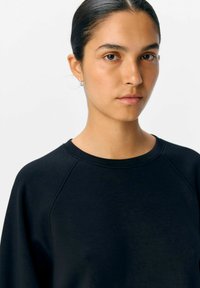 Sort sweatshirt med raglanærmer, blød tekstur og rund hals. Simpelt design uden mønstre eller betydelige hardware.