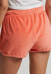 Pantaloni sportivi arancioni realizzati in un tessuto morbido e testurizzato, con una vita elastica, caratterizzati da una vestibilità ampia e un orlo curvo.
