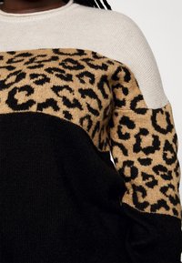 Megztinis su spalvų blokų dizainu: kreminė viršutinė dalis, smėlio spalvos su juodu leopardo raštu vidurinė dalis ir vienspalvė juoda apatinė dalis. Minkšta tekstūra.