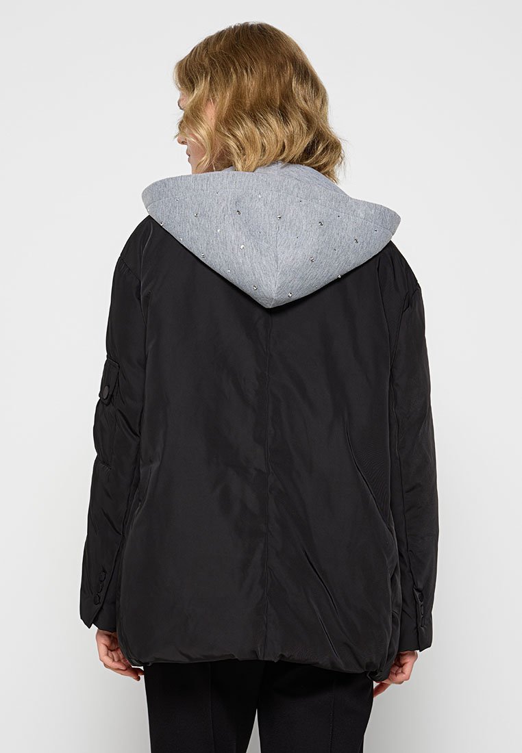 Schwarze Pufferjacke mit grauem Kapuzen. Sie hat eine gerippte Textur, einen subtilen Glanz und einen lockeren, übergroßen Schnitt. Die Kapuze verfügt über dekorative Elemente.