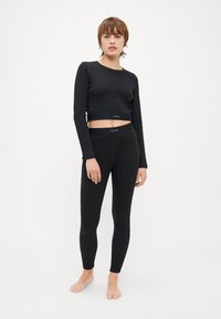 Svart langermet cropped topp og tights, laget av mykt, stretchy stoff. Begge har Calvin Klein-logo ved midjen.