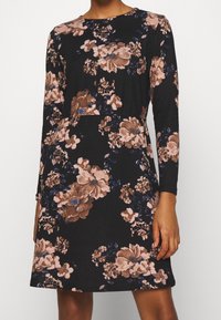 Czarna sukienka z długimi rękawami, zdobiona wzorem kwiatowym w odcieniach beżu i ciemnego niebieskiego. Miękka tkanina, lekko rozszerzany krój, okrągły dekolt.