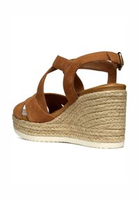 Sandalo con zeppa in suede marrone, con cinturini incrociati, punta aperta e tacco avvolto in juta intrecciata. Chiusura con cinturino alla caviglia.
