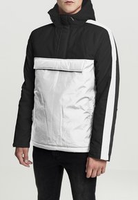 Padded jacket with a black upper and white lower section. Features a zippered front, a hood, and contrasting white side stripes.
