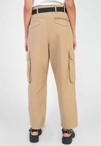 Beige cargobroek met twee zijzakken en twee achterzakken, voorzien van een zwarte riem. Gemaakt van een lichte stof met een ruime pasvorm.