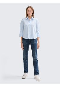 Chemise à rayures bleues et blanches avec col et manches trois-quarts, associée à un jean en denim bleu foncé et des baskets blanches.