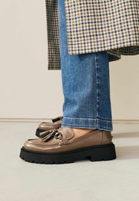 Bruna läderloafers med fransar, med en tjock svart sula. Bärs med blå raka jeans, vilket visar en avslappnad stil.