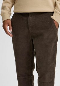 Pantaloni in corda marroni con una texture a coste verticali, tasche laterali e una vestibilità rilassata, abbinati a un maglione beige.
