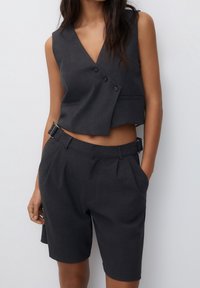 Szary krótki top z podwójnymi guzikami i bocznymi kieszeniami, zestawiony z szortami o wysokim stanie z zakładkami i detalem z klamrą.