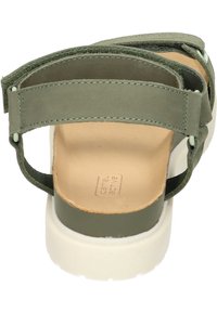 Sandale en daim vert avec semelle en caoutchouc blanc, brides ajustables et semelle intérieure rembourrée. Présente un dessus texturé et un design minimaliste.