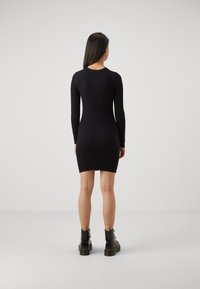 Svart ribbad långärmad klänning med en figursydd silhuett, som slutar vid mitten av låret, kombinerad med svarta snörade stövlar med kraftiga sulor och en markerad klack.