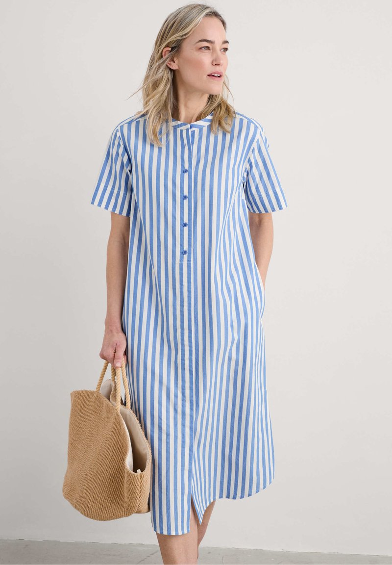 Abito a camicia a righe in blu e bianco, maniche corte, con bottoni davanti, realizzato in tessuto leggero. Include tasche, abbinato a una borsa intrecciata.