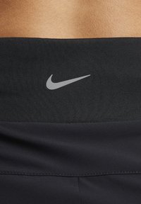 Primer plano de una cinturilla atlética negra con el logotipo plateado reflectante de Nike en un fondo de piel desnuda.