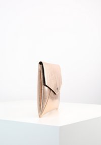 Metallinen ruusukultainen clutch-laukku, jossa on kolmiomainen keskiö ja nappisuljenta. Silkkinen pinta ja hoikka muotoilu, seisoo pystyssä valkoisella pinnalla.