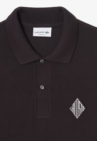 Čierne polokošeľa s textúrovaným vzorom, dvoma gombíkmi a bielym vyšitým logom v tvare diamantu na ľavej strane hrudníka. Klasický strih.