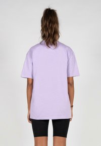 Lavendelfarbenes Baumwoll-T-Shirt mit lockerer Passform, kurzen Ärmeln und Rundhalsausschnitt, getragen mit schwarzen Shorts. Einfaches Design, keine sichtbaren Muster.