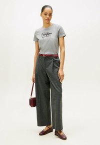 Grå bomulds T-shirt med "Hilfiger" logo, parret med højtaljede grå stribede bukser, bordeaux bælte og matchende håndtaske. Brune flade sko.