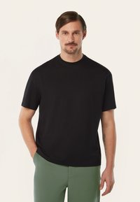 Zwarte korte mouwen T-shirt met ronde hals, gemaakt van gladde katoenstof; gecombineerd met groene broeken. Geen zichtbare patronen of accenten.