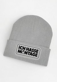 Gray knit beanie with a ribbed texture, featuring a large rectangular patch that reads “¡ICH HASSE MONTAGE!” in bold black letters.