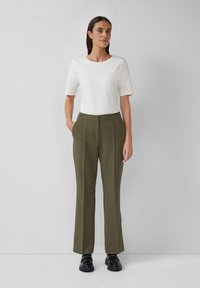 Maglietta bianca a maniche corte e pantaloni tailored verde oliva. I pantaloni presentano tasche laterali e una vestibilità dritta. Scarpe nere completano l'outfit.