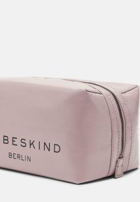 Borsa cosmetica rosa con forma rettangolare, materiale nylon liscio, marchiata "BESKIND BERLIN," con una cerniera argentata e dettagli di cucitura.