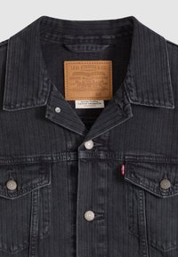 Μαύρο τζιν μπουφάν με σχέδιο ψαροκόκκαλο, ασημένια κουμπιά και ετικέτα από καφέ δέρμα. Διαθέτει δύο τσέπες στο στήθος και μυτερό γιακά.