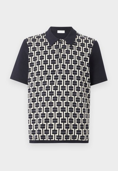 Πολο με κοντά μανίκια σε ναυτικό μπλε χρώμα με γεωμετρικό λευκό μοτίβο εμπλεκόμενων τετραγώνων μπροστά και μονόχρωμα μανίκια. Τρία κουμπιά στην πατιλέτα.