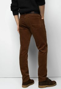 Brown corduroy pants with a slim fit, featuring two back pockets and a textured surface, paired with dark brown ankle boots.