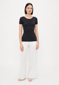 Black fitted t-shirt with a round neckline, paired with white wide-leg pants. Fabric appears smooth, with a lightweight and stretchy texture.