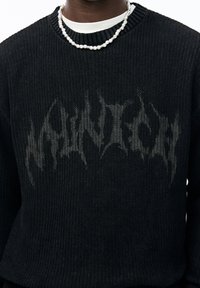 Pull noir en maille avec un grand logo gris "Munich" en travers de la poitrine. Encolure ronde et texture côtelée sur l'ensemble.
