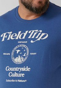 Niebieska bawełniana koszulka z białym nadrukiem tekstu i grafik, w tym "Wyprawa w teren", okrągła scena przyrody oraz różne hasła.
