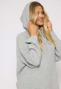 Sudadera gris con una textura suave, capucha con cordones y un ajuste relajado. Presenta mangas anchas y un diseño casual.