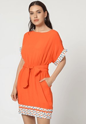 Vestido naranja con mangas cortas, que presenta una cintura ceñida con cinturón, bolsillos laterales y puños decorados con un diseño de azul, naranja y blanco en el dobladillo.