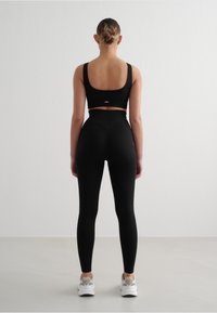 Schwarzer Rippensport-BH und hoch geschnittene Leggings, mit einer enganliegenden Passform, glatter Textur und minimalem Branding am Bund.