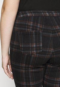 Mustapekka ja harmaan ruutukuosiset housut oranssilla rekvisiitalla, joissa on takatasku ja mukautettu malli. Tekstuuri näyttää sileältä ja hieman joustavalta.