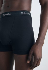Fekete pamut boxer alsónemű, puha elasztikus derékkal, melyen a "Calvin Klein" logó világos színben található. Simára kialakított textúra, testre simuló dizájn.