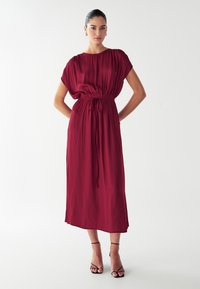 Vestido maxi burdeos en un tejido ligero, con cintura ceñida, mangas cortas tipo volante y una falda recta con una textura suave.