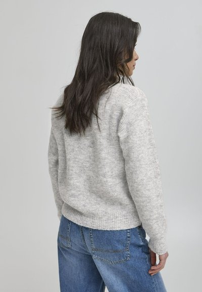Lysegrå strikket genser med ribbestruktur, rund hals, og en noe oversized passform, paret med blå denimjeans.